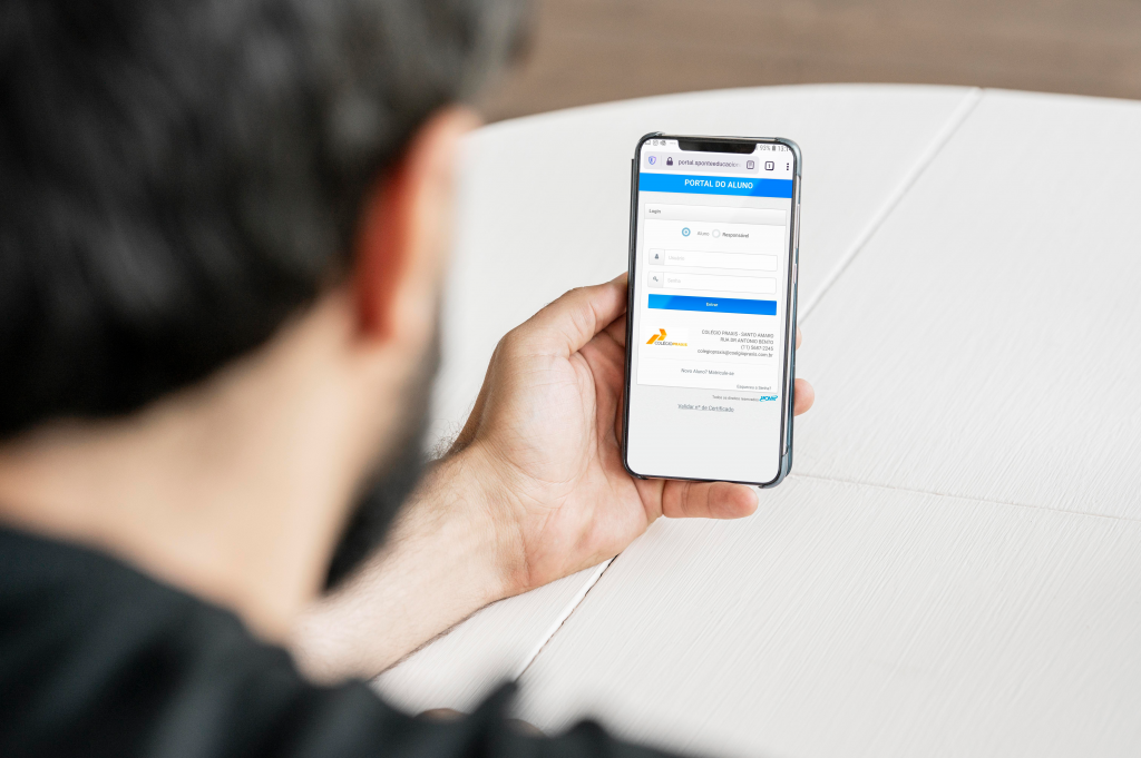 Homem usando um celular com a área do aluno do colégio praxis